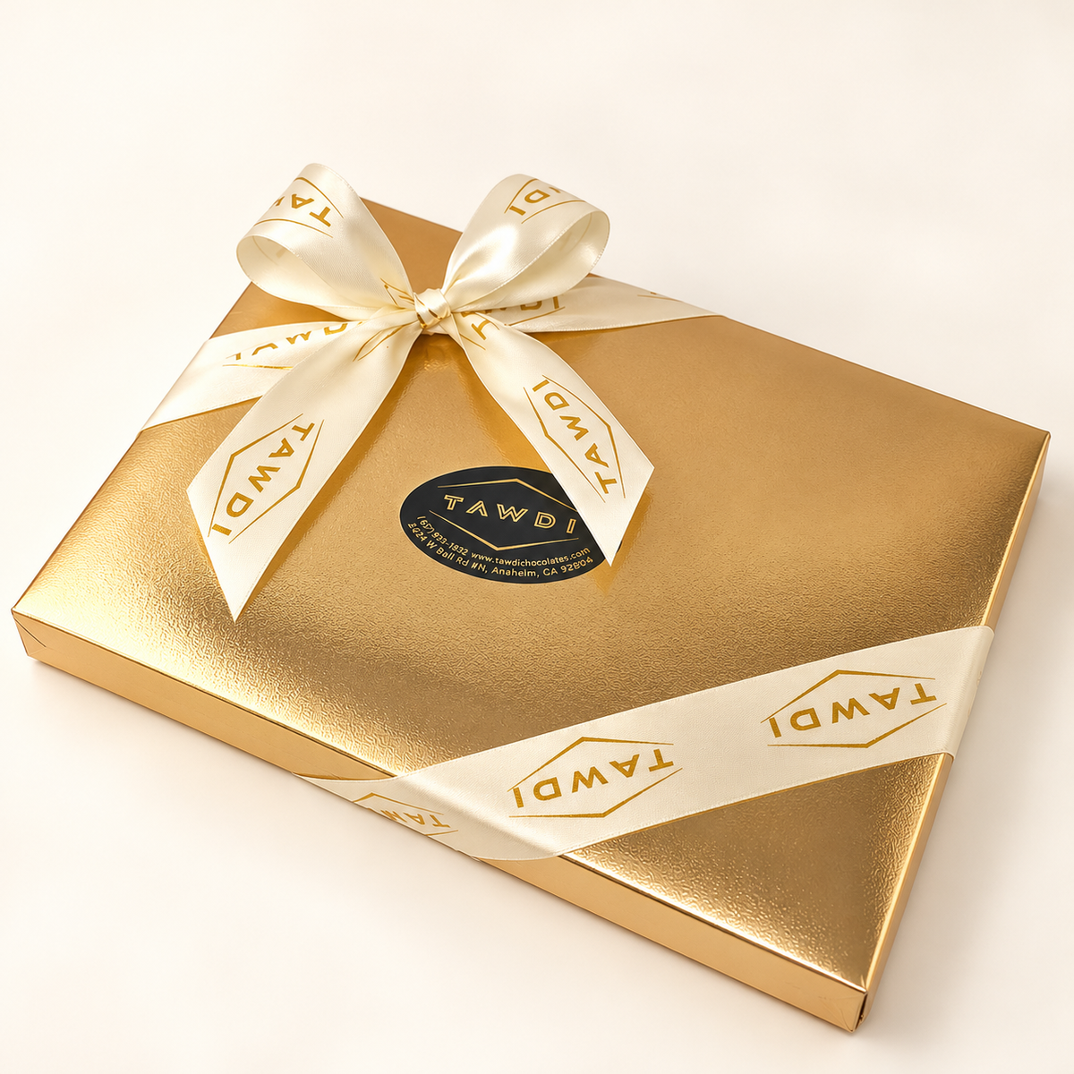 TAWDI Signature Box in gold with a cream TAWDI ribbon, closed